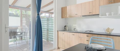 A modern kitchen with wooden cabinets, a dining table set with plates and glasses, and a view through a glass door to an outdoor deck.