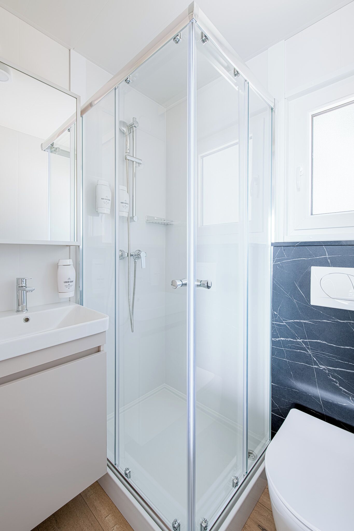 A modern bathroom with a glass-enclosed shower, a white sink, and a marble-tiled wall.