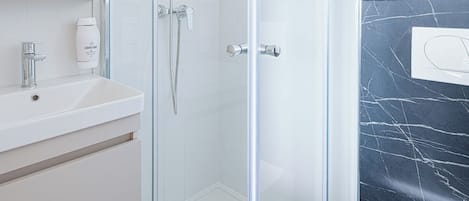 A modern bathroom with a glass-enclosed shower, a white sink, and a marble-tiled wall.