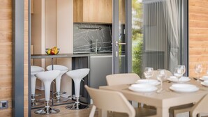 Een moderne keuken met een marmeren aanrecht, houten kastjes en een glazen deur naar een eethoek met witte barkrukken en een gedekte tafel.