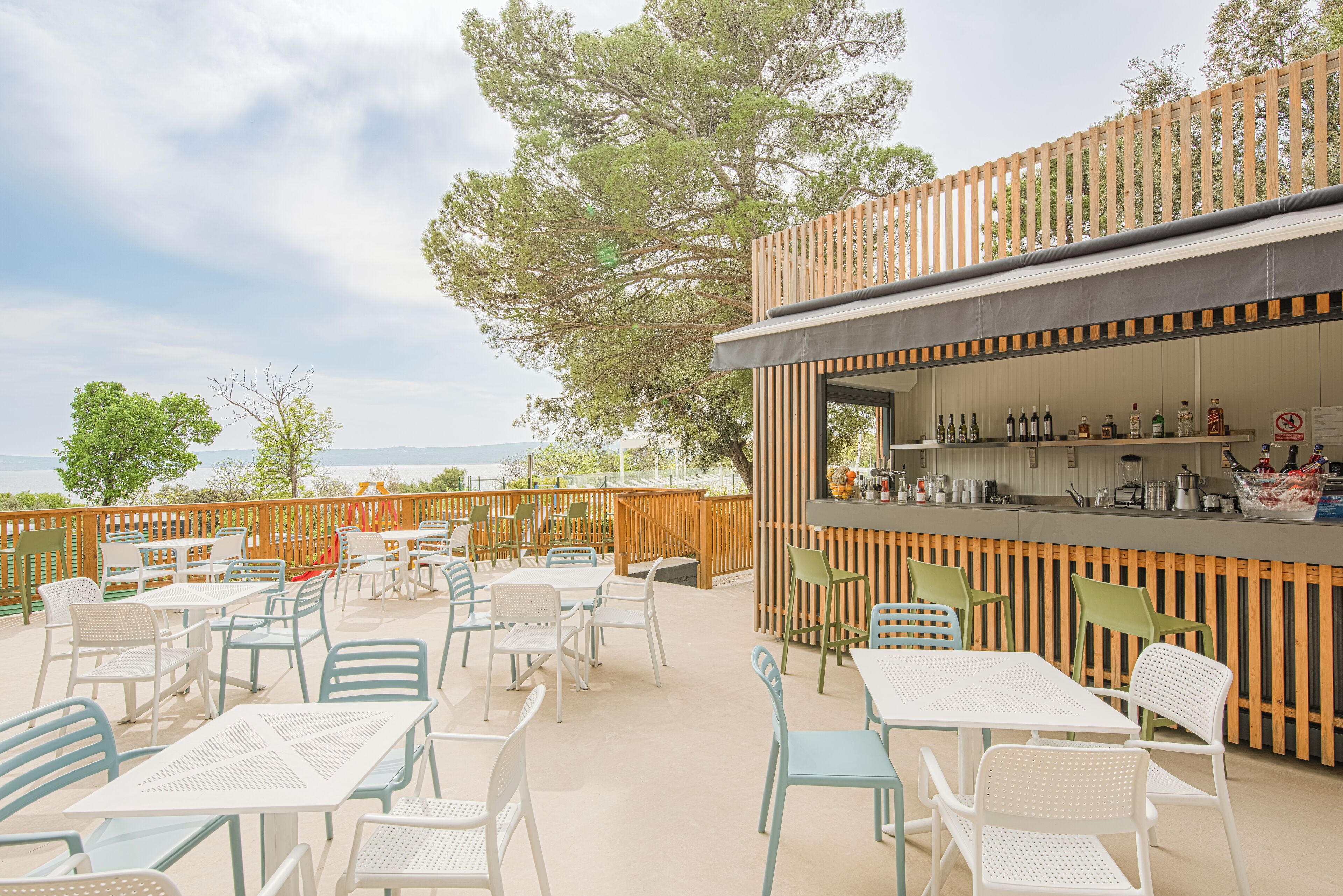 Een terras buiten met tafels, stoelen, een bar en uitzicht op de zee.