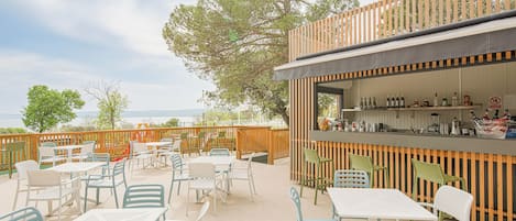 An outdoor patio area with tables and chairs, a bar counter, and a view of the sea.