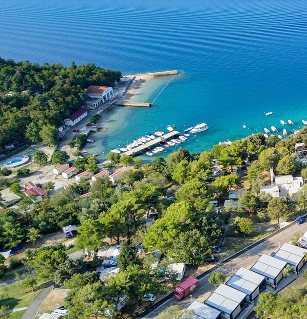 Vue aérienne d’une zone côtière comprenant un port de plaisance, plusieurs bateaux amarrés et un mélange de bâtiments résidentiels et commerciaux.