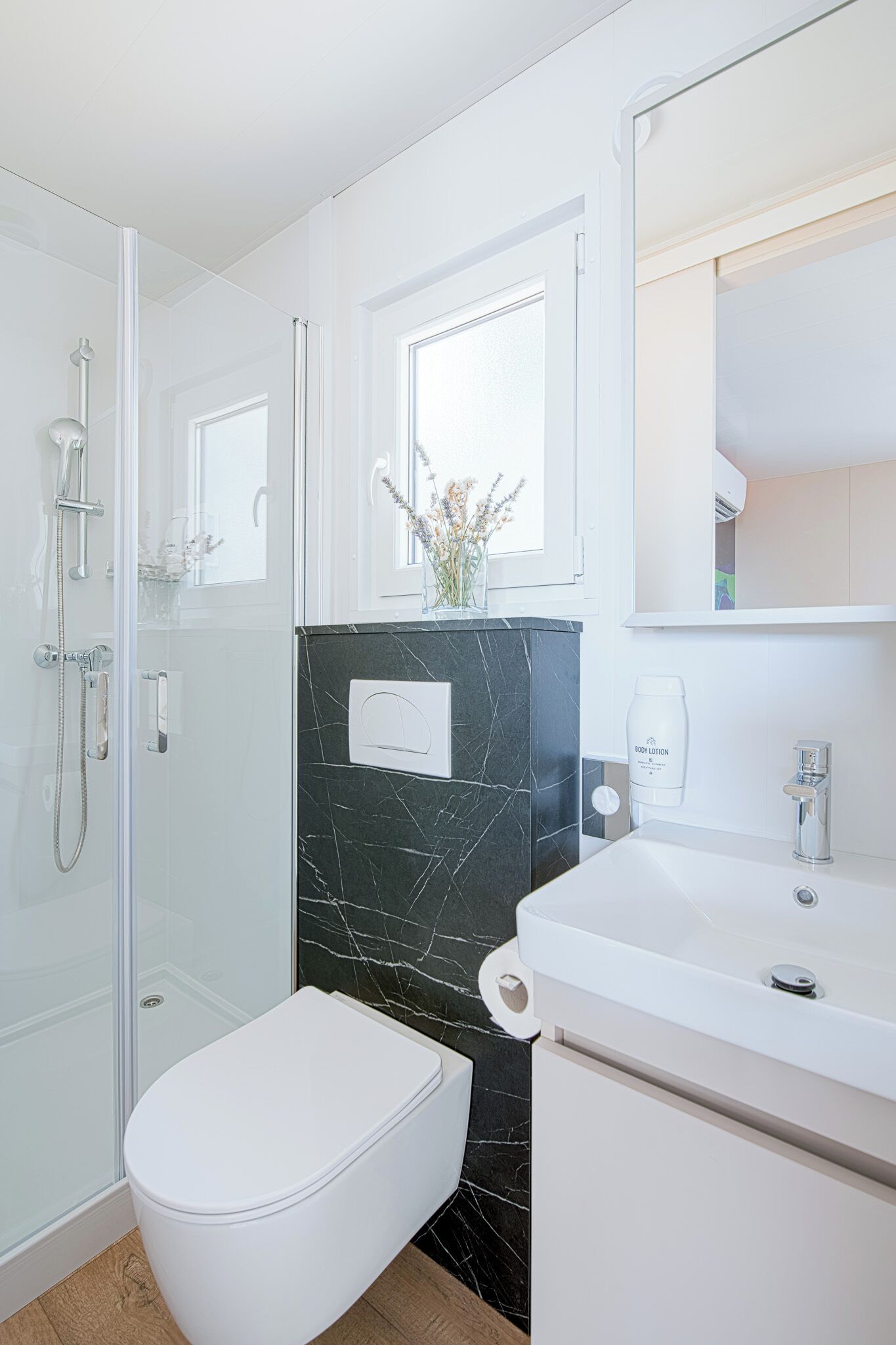 Une salle de bain moderne avec des toilettes blanches, un lavabo en marbre noir et une douche à parois de verre.