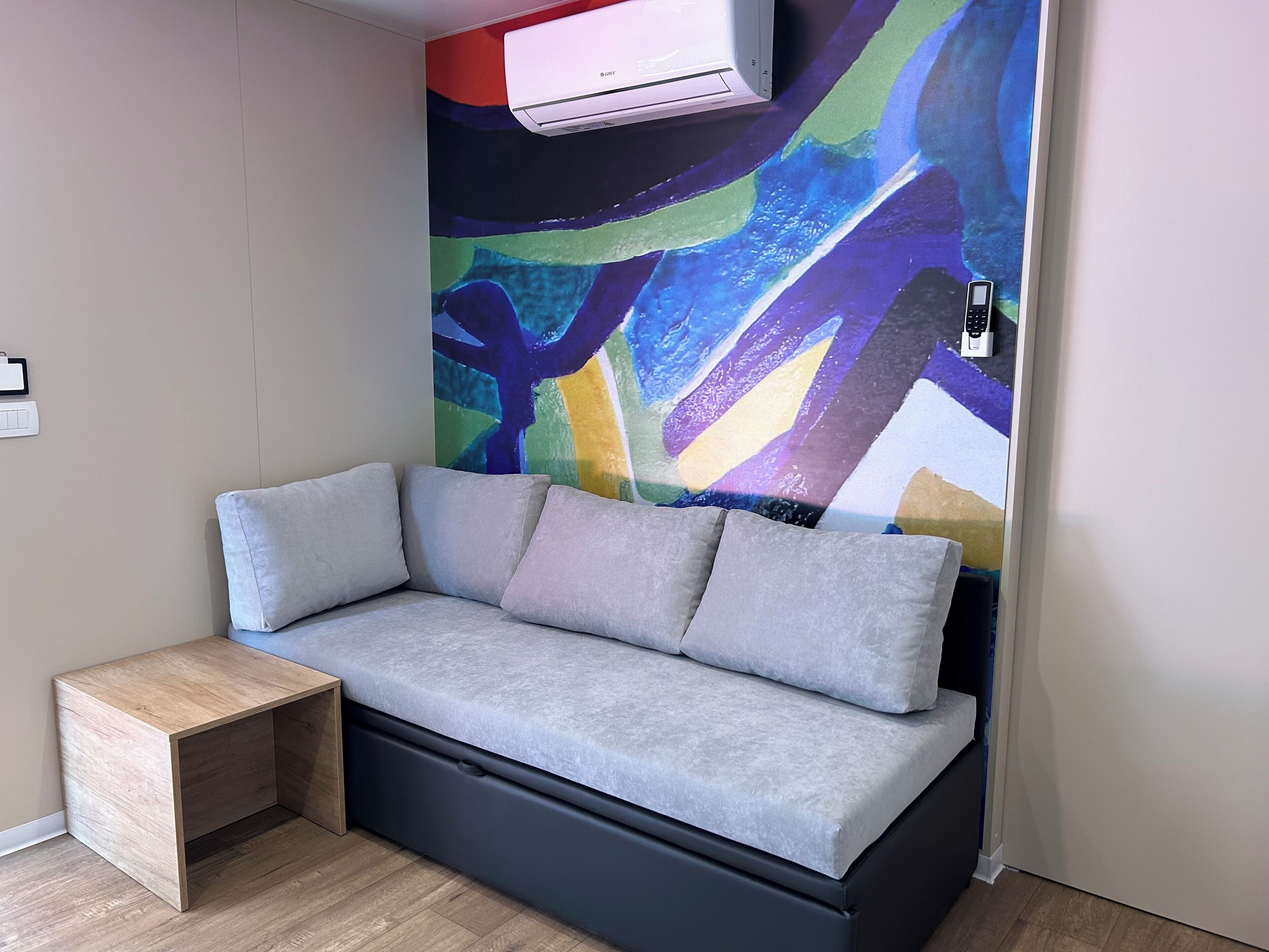 A modern room with a grey sofa, a small wooden side table, and a colorful abstract wall mural.