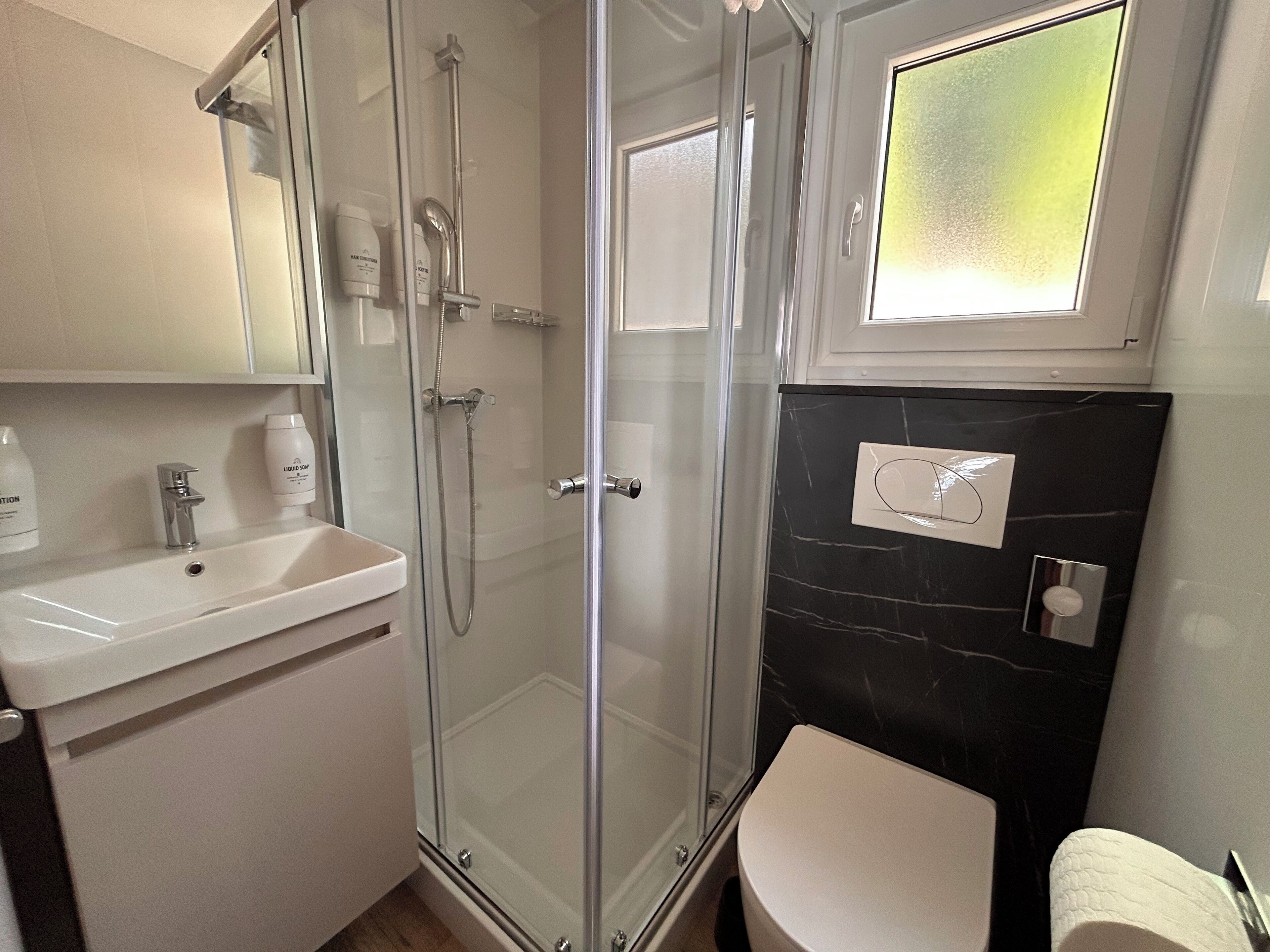 Une salle de bain moderne avec une douche à parois de verre, un lavabo blanc et un mur en marbre noir.