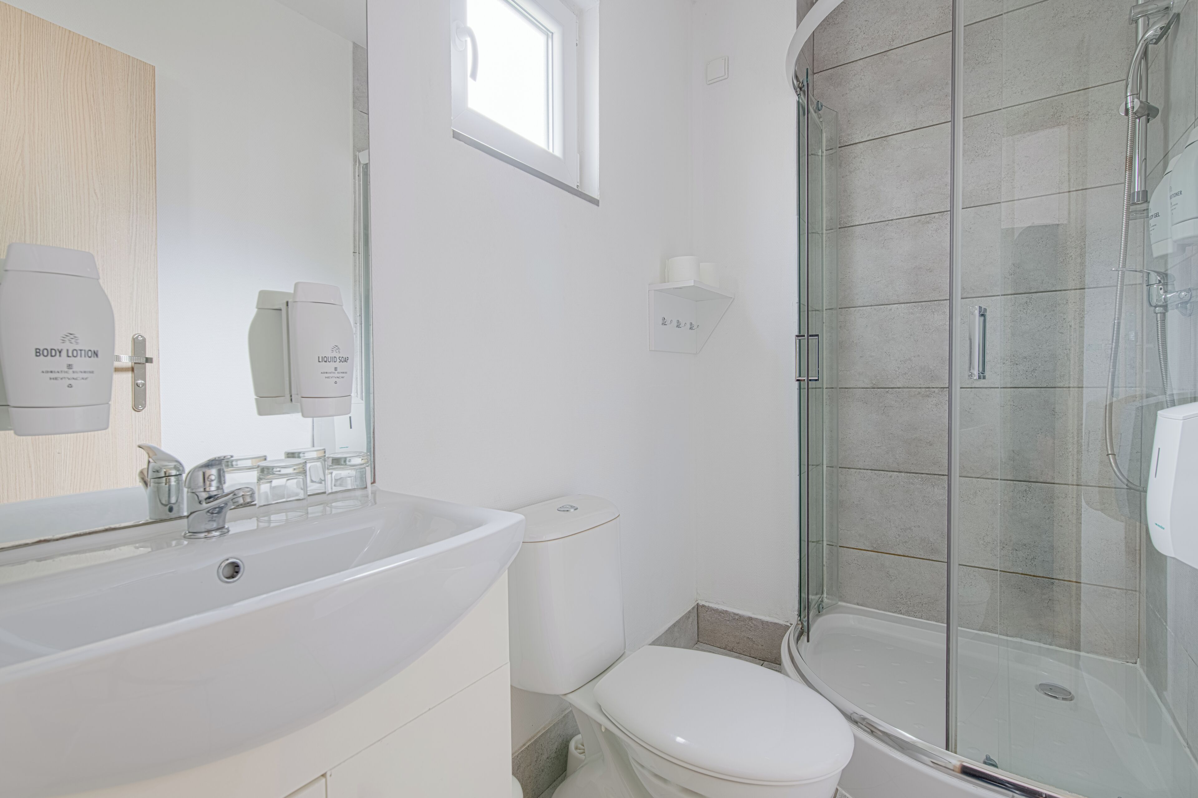 A modern bathroom with a large white sink, a toilet, and a glass-enclosed shower.