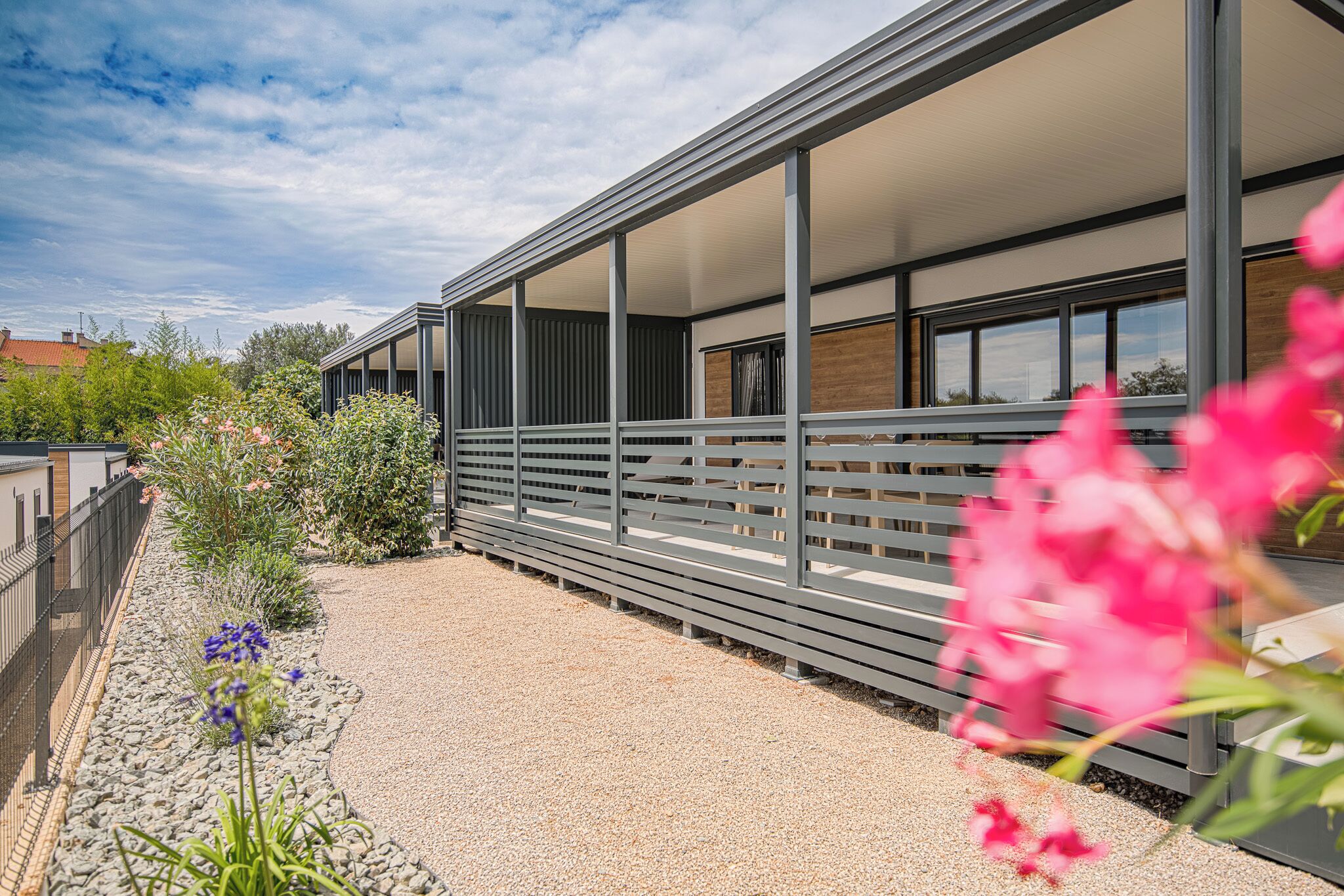A modern building with a covered outdoor area, a gravel path, and various plants.