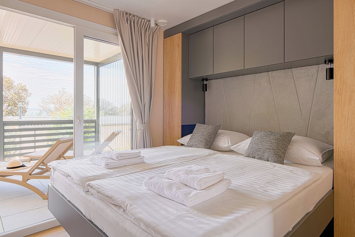 Una habitación de hotel moderna con una cama grande, dos almohadas y vistas al exterior.
