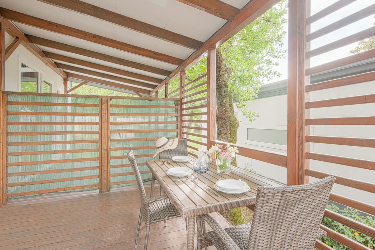 Una terraza exterior de madera con una mesa dispuesta para comer, rodeada de sillas de mimbre.