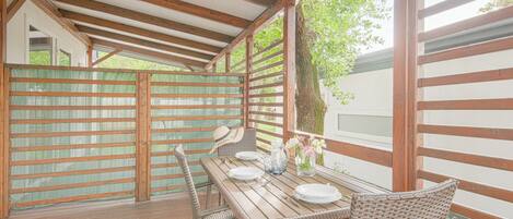 Una terraza exterior de madera con una mesa dispuesta para comer, rodeada de sillas de mimbre.