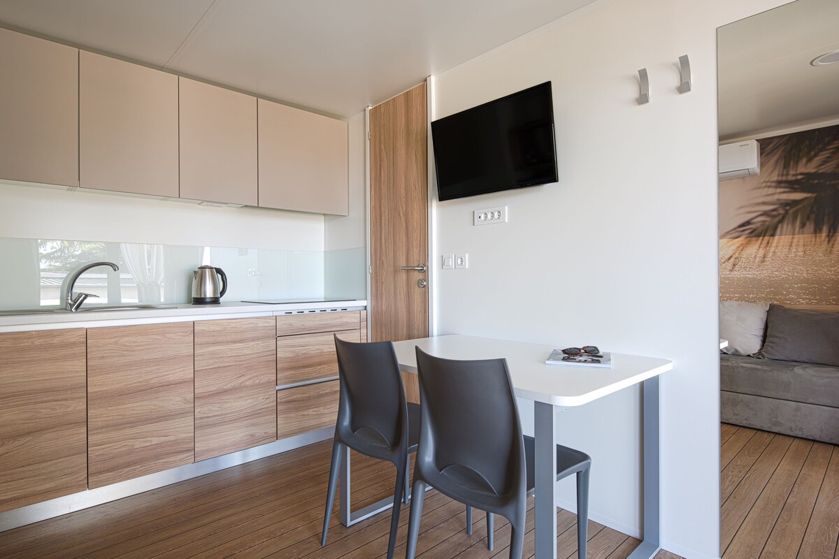 Une cuisine moderne avec des meubles en bois, un plan de travail blanc et un téléviseur à écran plat fixé au mur.