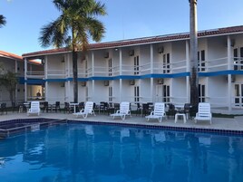 Un hotel con piscina, sillones de descanso y una palmera.