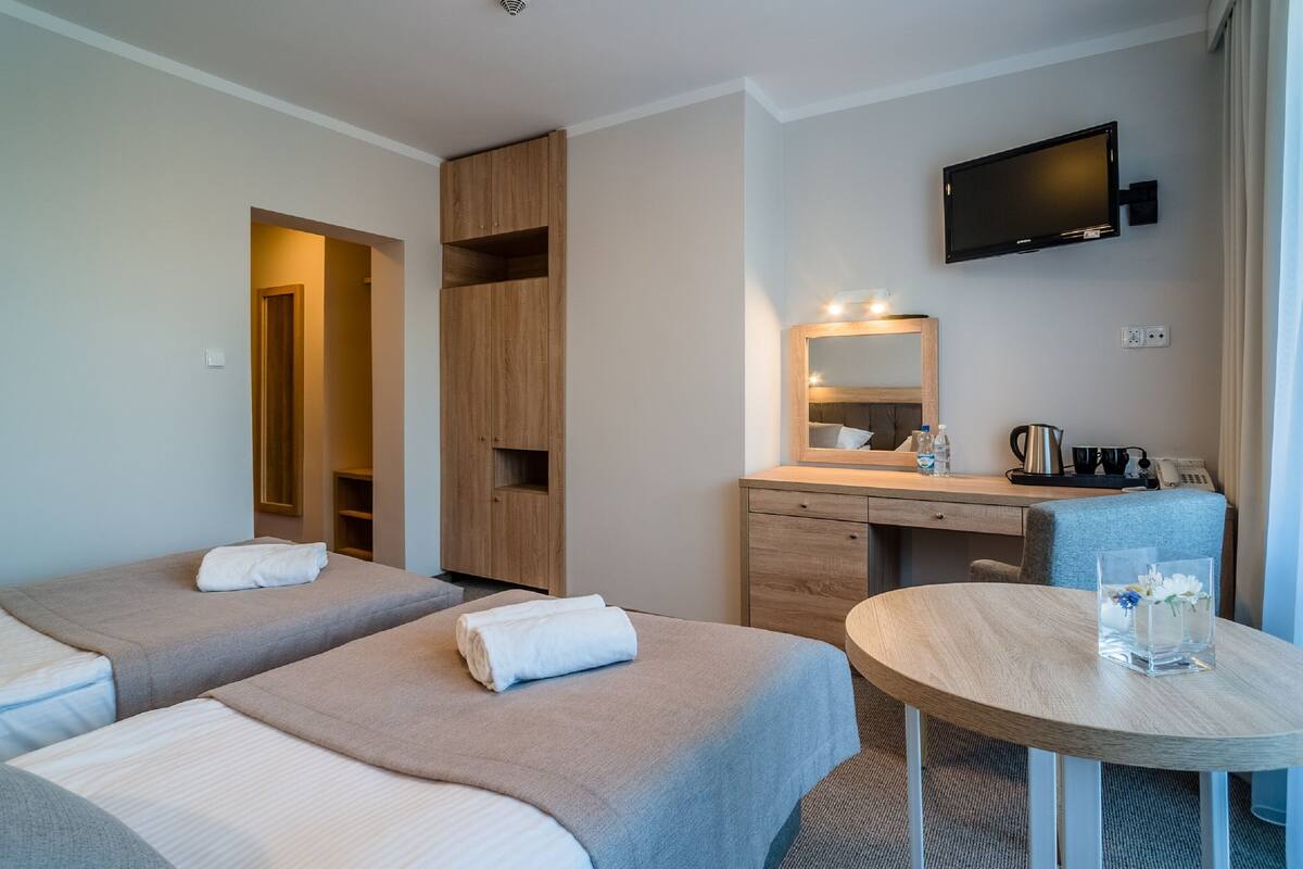 Une chambre d’hôtel avec deux lits, un bureau, une chaise, une télévision et une petite table sur laquelle se trouve un vase.