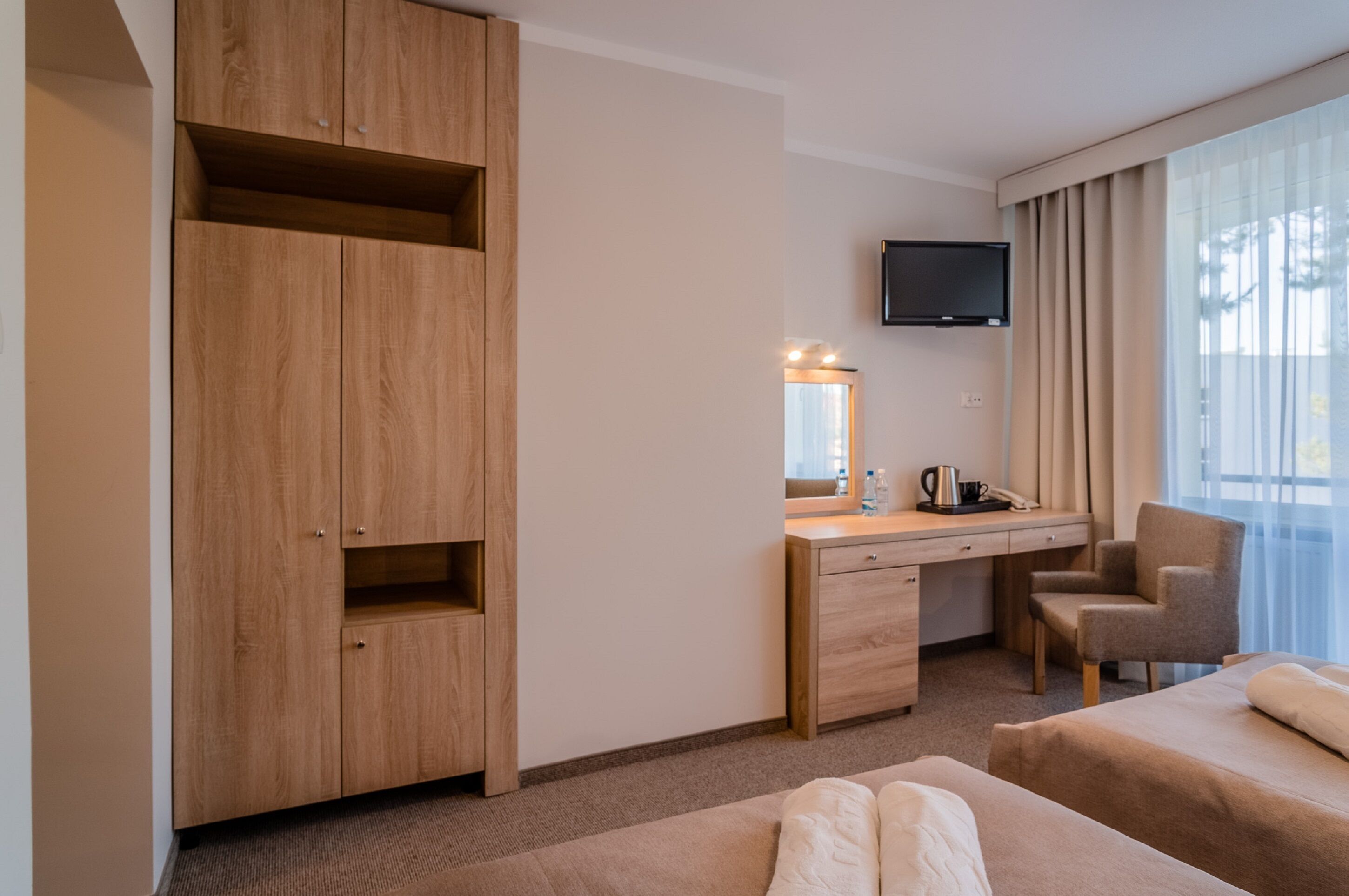 Une chambre d’hôtel avec une armoire en bois, un bureau avec un miroir, une chaise, un lit et un téléviseur fixé au mur.