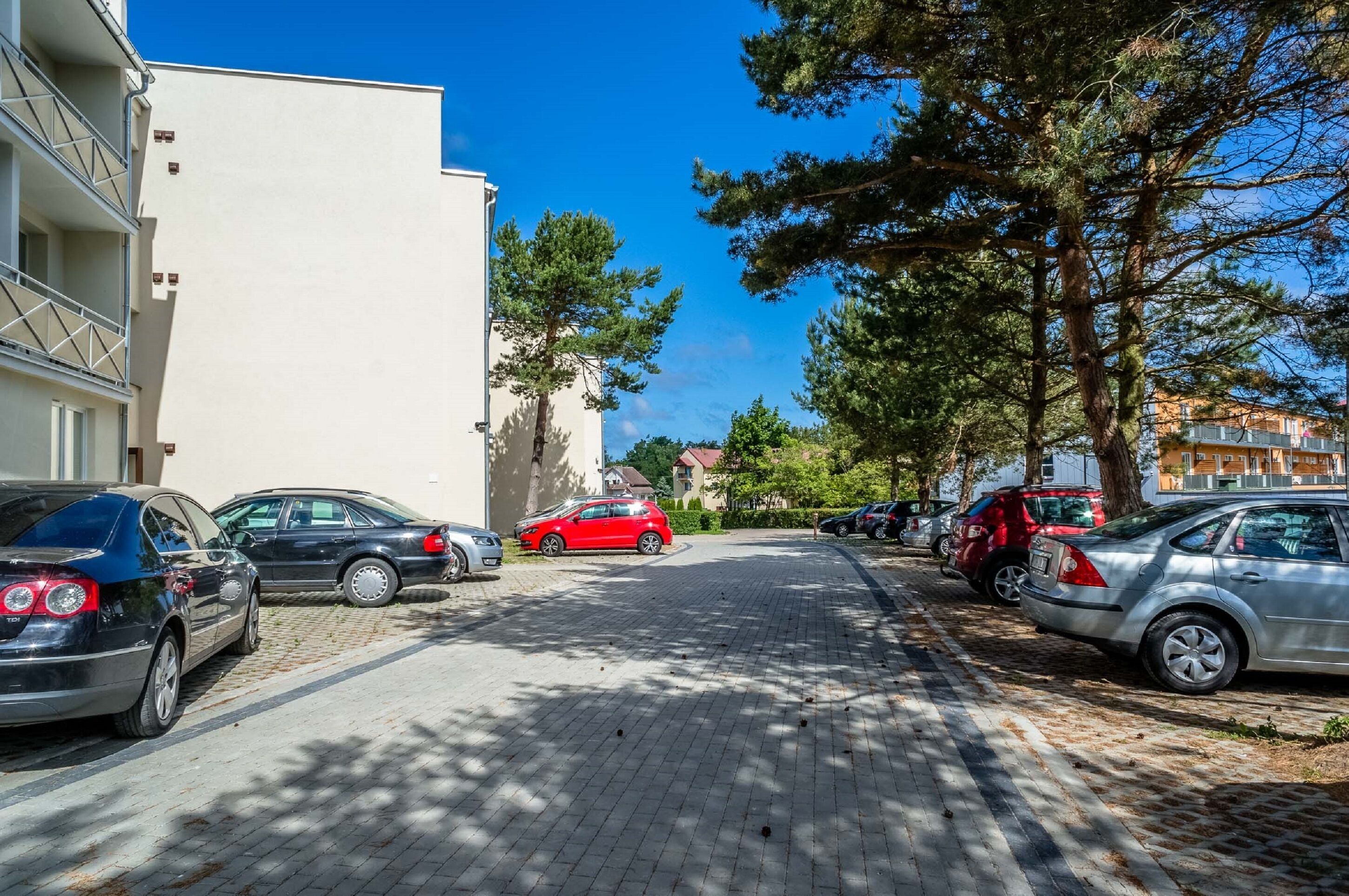 Eine Straße gesäumt von parkenden Autos und Bäumen, mit Gebäuden an beiden Seiten.
