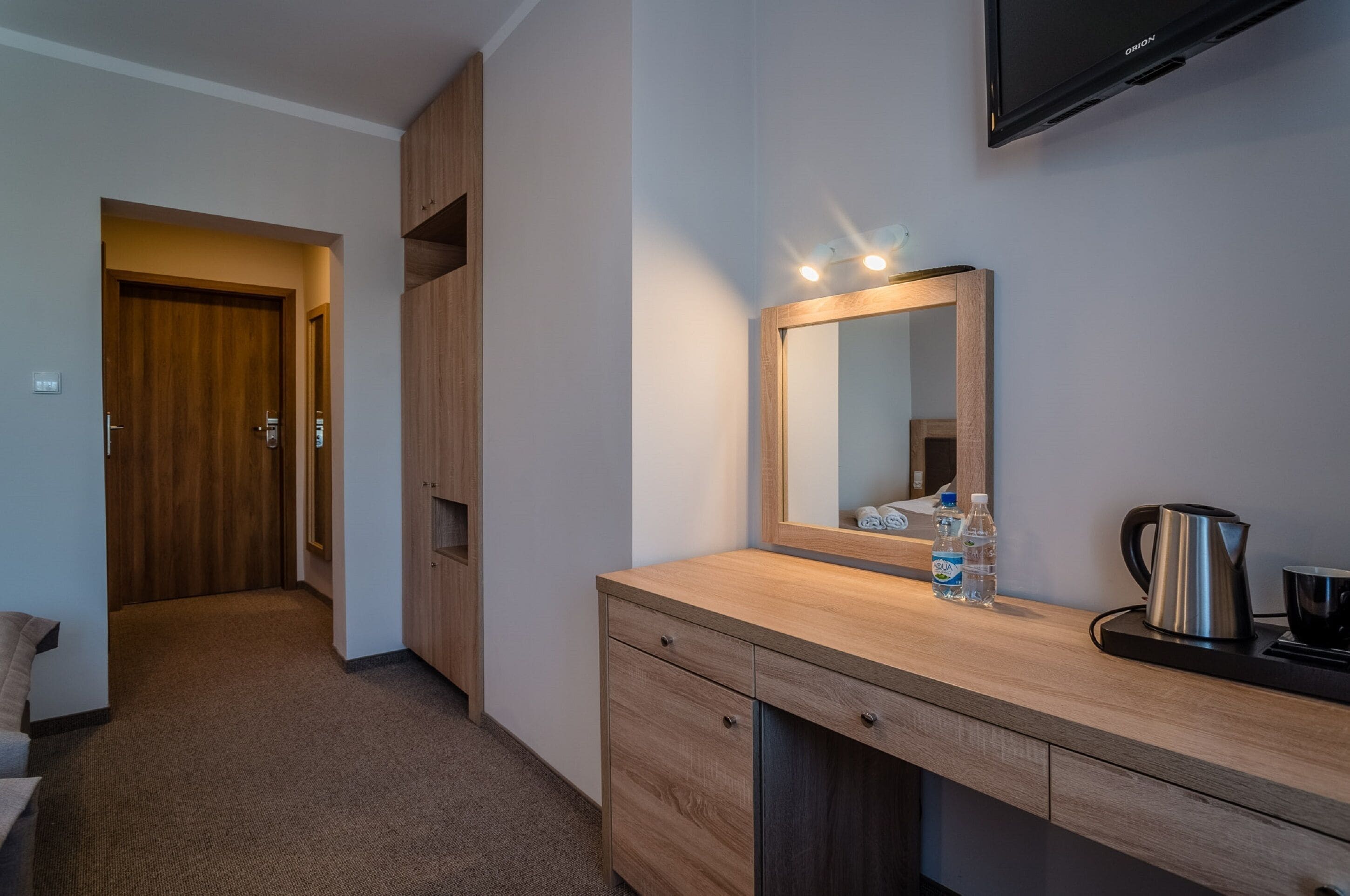 A modern bathroom with a wooden vanity, a mirror, a sink, and a television mounted on the wall.