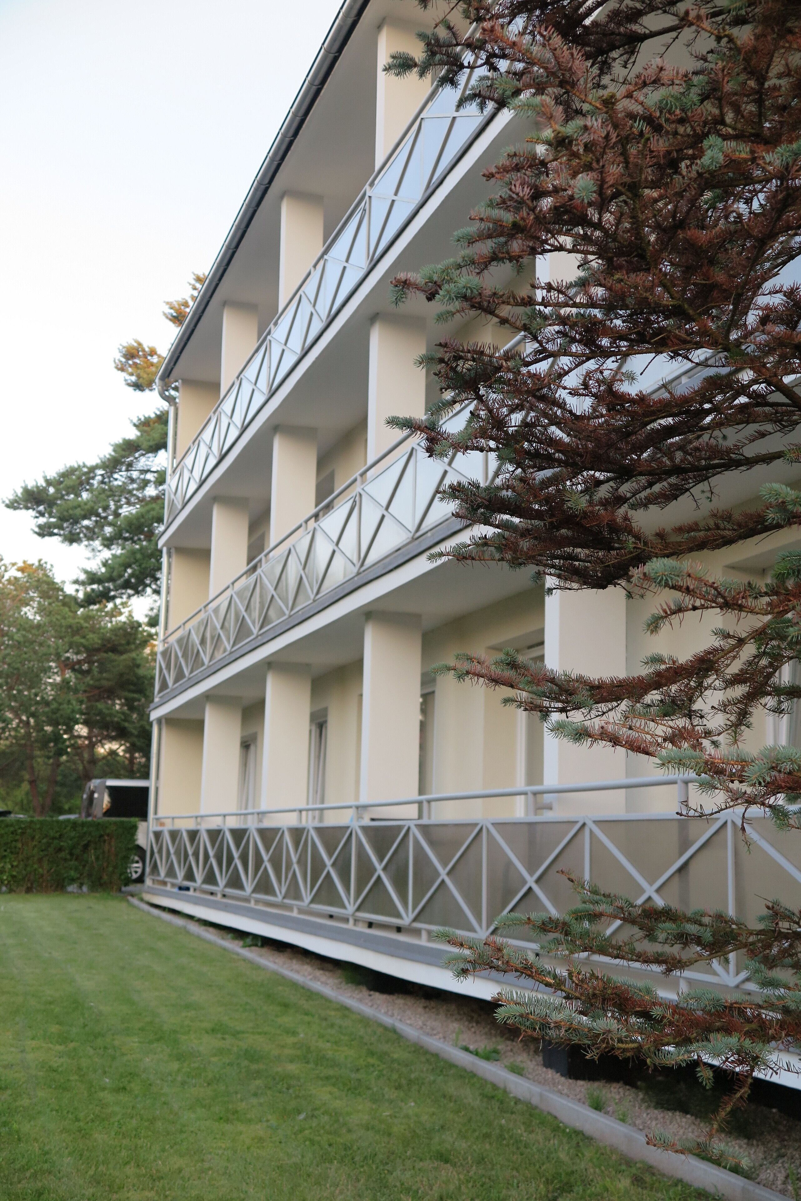 Un edificio de varios pisos con un balcón y un árbol frente a él.