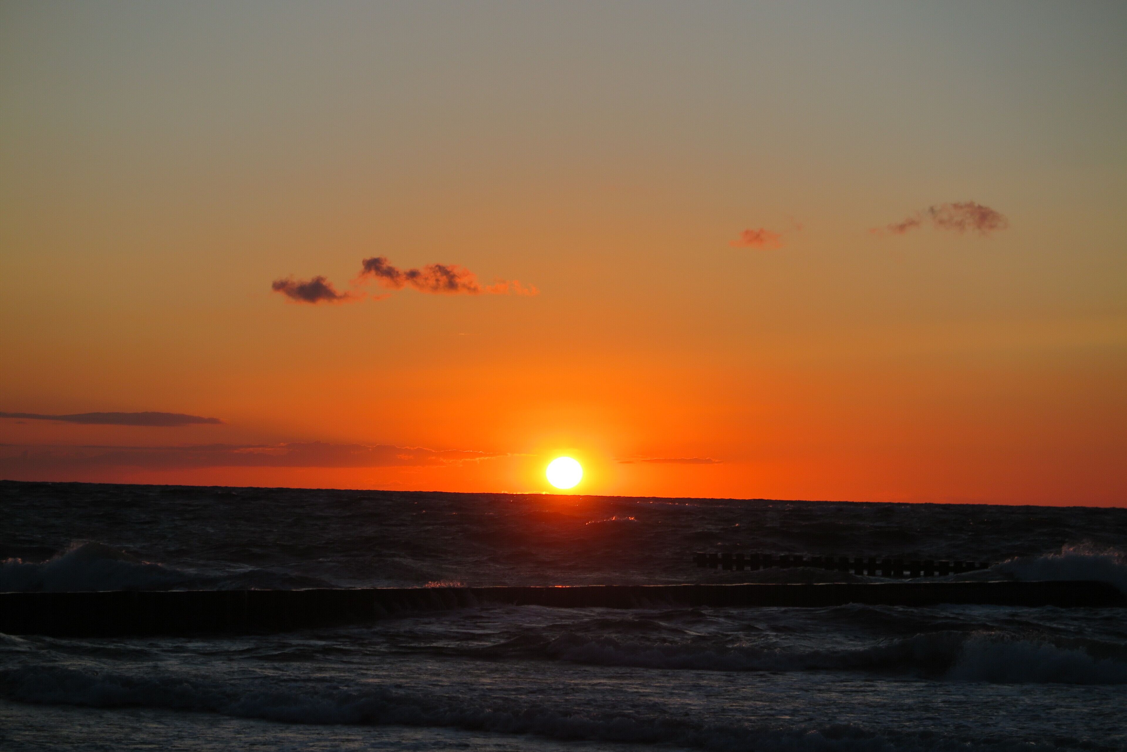 Een zonsondergang boven de oceaan, met golven die op een pier breken.