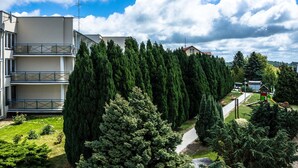 A residential building with a balcony, surrounded by tall evergreen trees and a small playground. - Hotel NAT Jaroslawiec (Postomino)