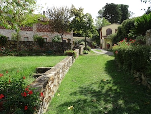A stone wall with a grassy area and red flowers in front of a building with a stone facade and windows.