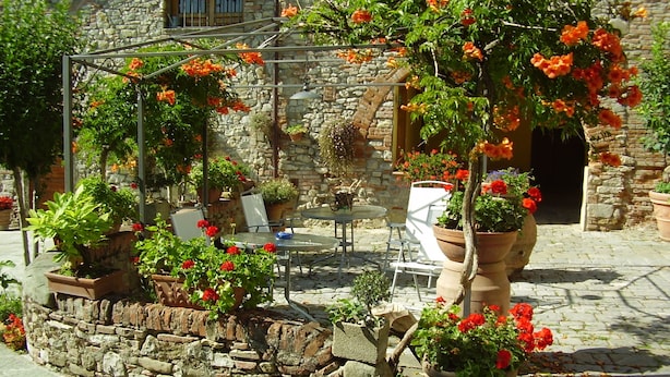 Ein Hof aus Stein mit Außenbestuhlung, Pflanzkübeln und einer Pergola.