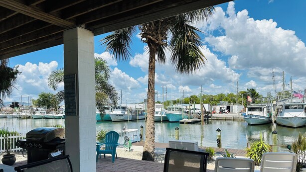 Un espace extérieur aménagé, abrité et doté de sièges, offrant une vue sur un port de plaisance et des bateaux.