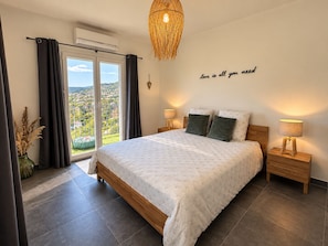 Une chambre avec un lit, deux lampes de chevet, un luminaire fixé au mur, une vue à travers une porte coulissante et une citation décorative sur le mur.