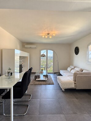 Una sala moderna con una mesa de comedor de vidrio, un sofá y vistas al exterior.