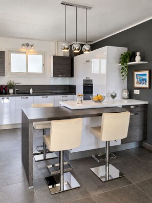 A modern kitchen with a central island, bar stools, and pendant lighting.