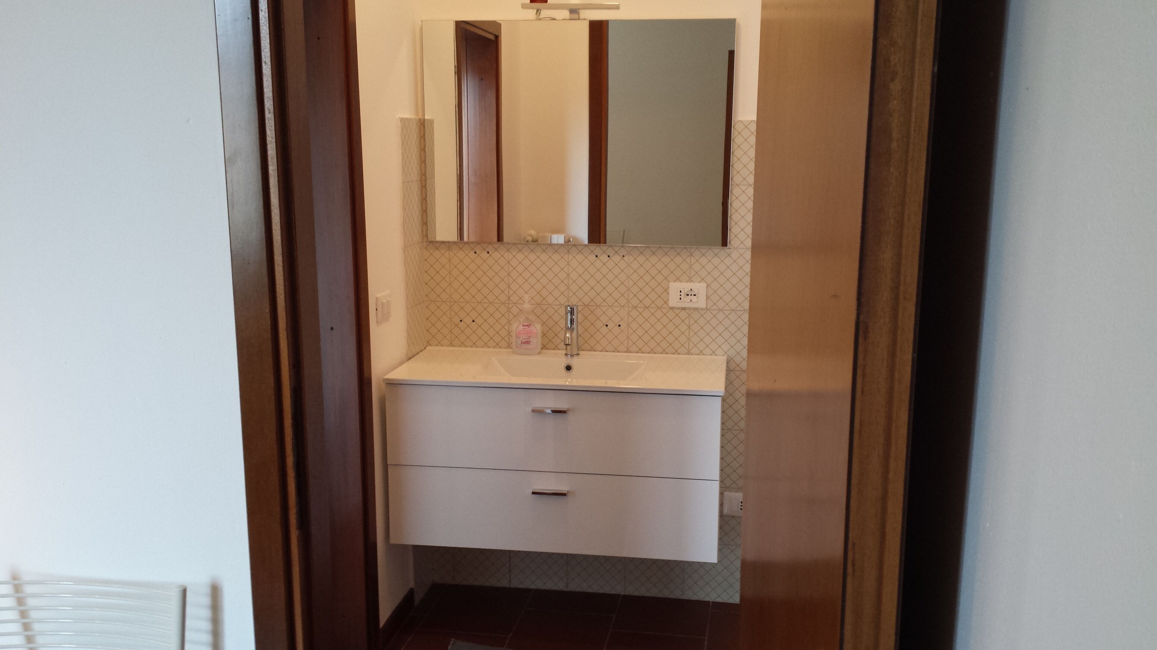 Un baño con un lavamanos blanco, un espejo encima y un salpicadero de azulejos.