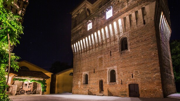A historic brick building with arched windows and a bell tower, illuminated at night. - Palazzo Barbò (Torre Pallavicina)