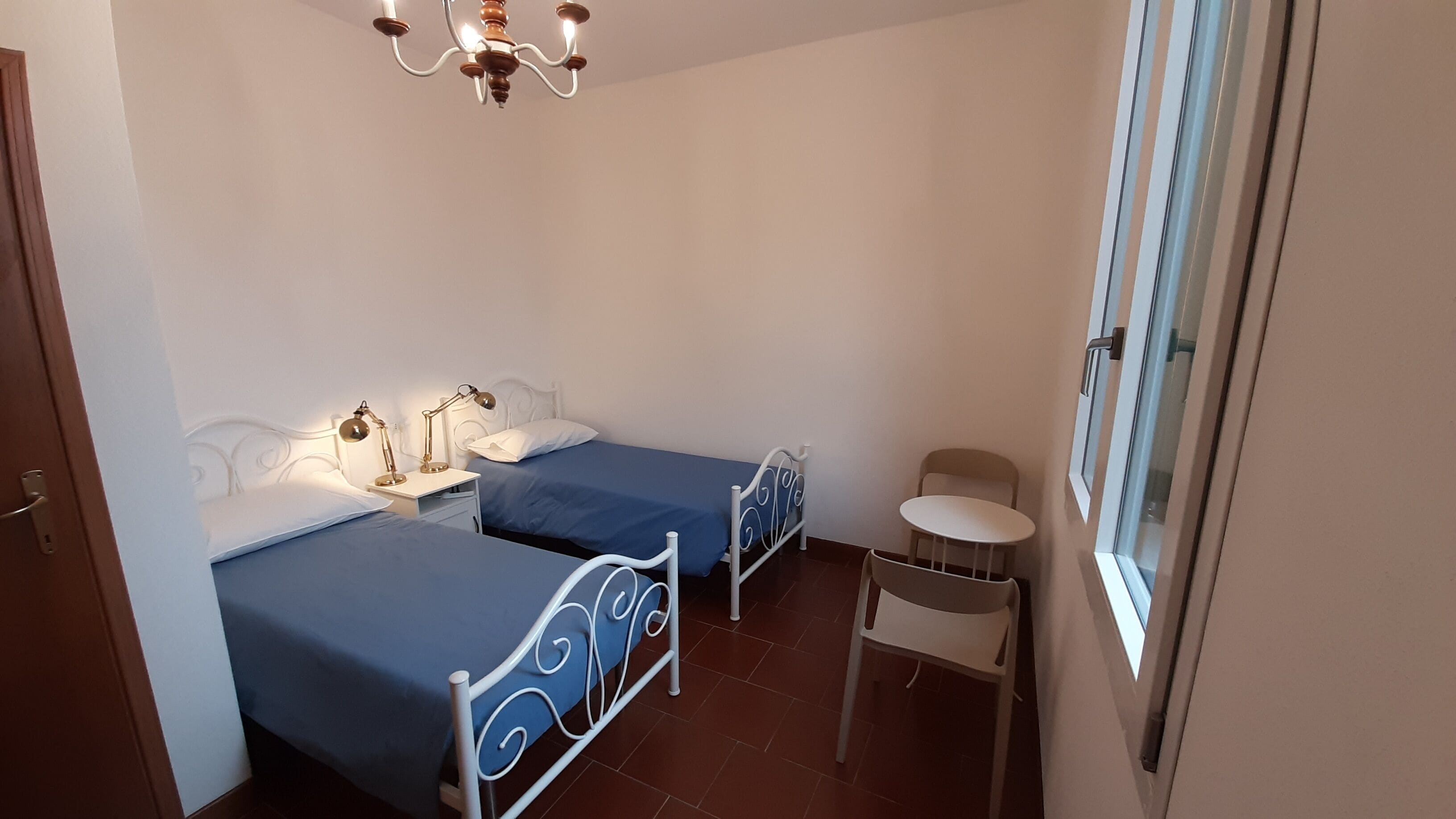 A bedroom with two beds, a small table, a chair, and a window.