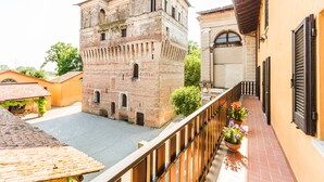 A courtyard with a historic brick tower, a tiled roof, and a balcony with potted plants. - Palazzo Barbò (Torre Pallavicina)