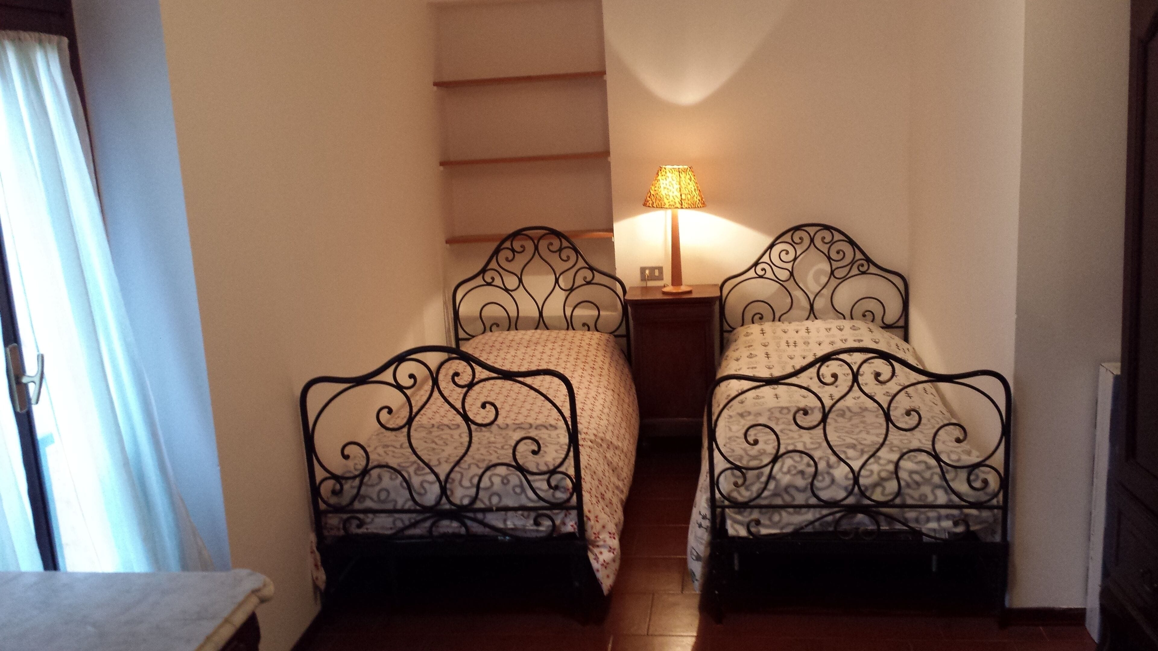 Une petite pièce avec deux lits en métal, dotés de draps à motifs, une petite table et une lampe sur une table de chevet.