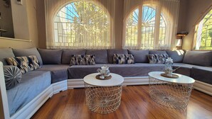 A modern living room with a grey sectional sofa, two round coffee tables, and large arched windows with sheer curtains.