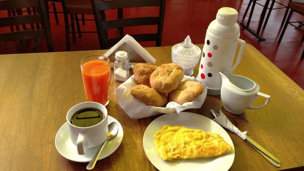 Um café da manhã com uma xícara de café, um copo de suco de laranja, um prato de doces, uma omelete pequena e um jarro.