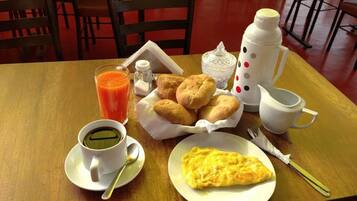 Um café da manhã com uma xícara de café, um copo de suco de laranja, um prato de doces, uma omelete pequena e um jarro.
