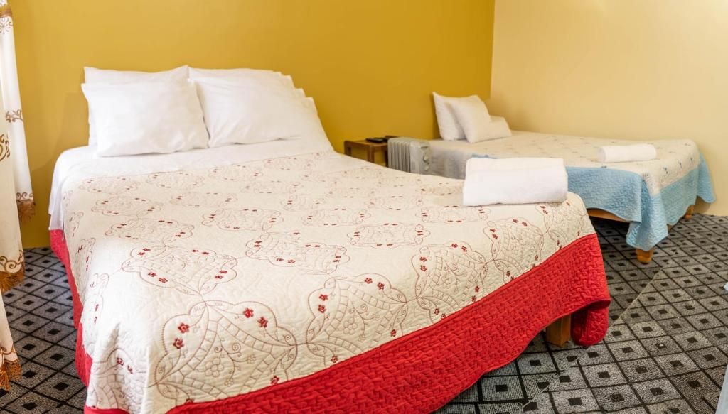 A hotel room with a large bed, two smaller beds, a nightstand, and a patterned bedspread.