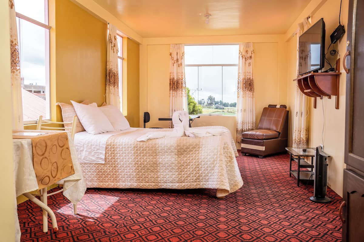 A hotel room with a bed, a chair, a table, and a TV.