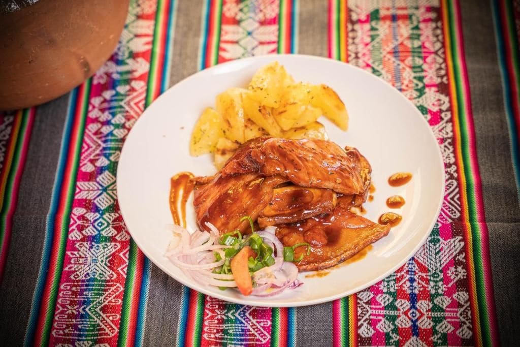 Ein Teller Essen mit einem Hähnchenschenkel, Ananasstücken und einem Beilagensalat auf einer farbenfrohen gewebten Tischdecke.