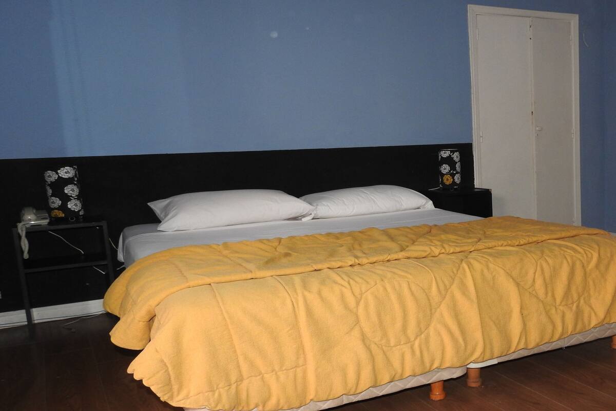 Quarto com cama, mesa de cabeceira e porta.