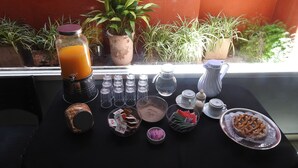 Ein Frühstückstisch mit einem Fruchtsmoothie, Kaffeekannen, Zucker, Teebeuteln und einer Auswahl an Gebäck.