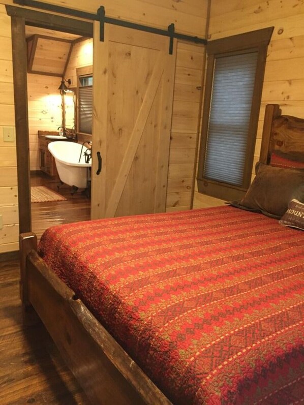 Un dormitorio tipo cabaña de madera con cama, una ventana con persianas y un baño con bañera.