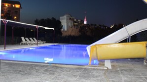 Uma piscina com escorregador, cadeiras de descanso e um edifício com cúpula ao fundo.