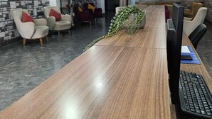 Uma área de recepção com um balcão comprido de madeira, várias cadeiras, um vaso de planta e uma parede com padrão de pedra.