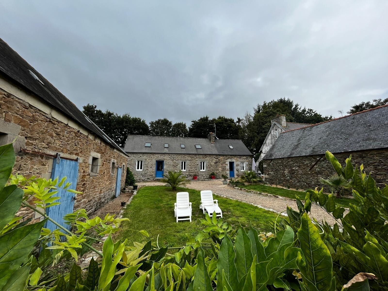 A stone building with a grassy courtyard, two blue doors, and white lounge chairs.
