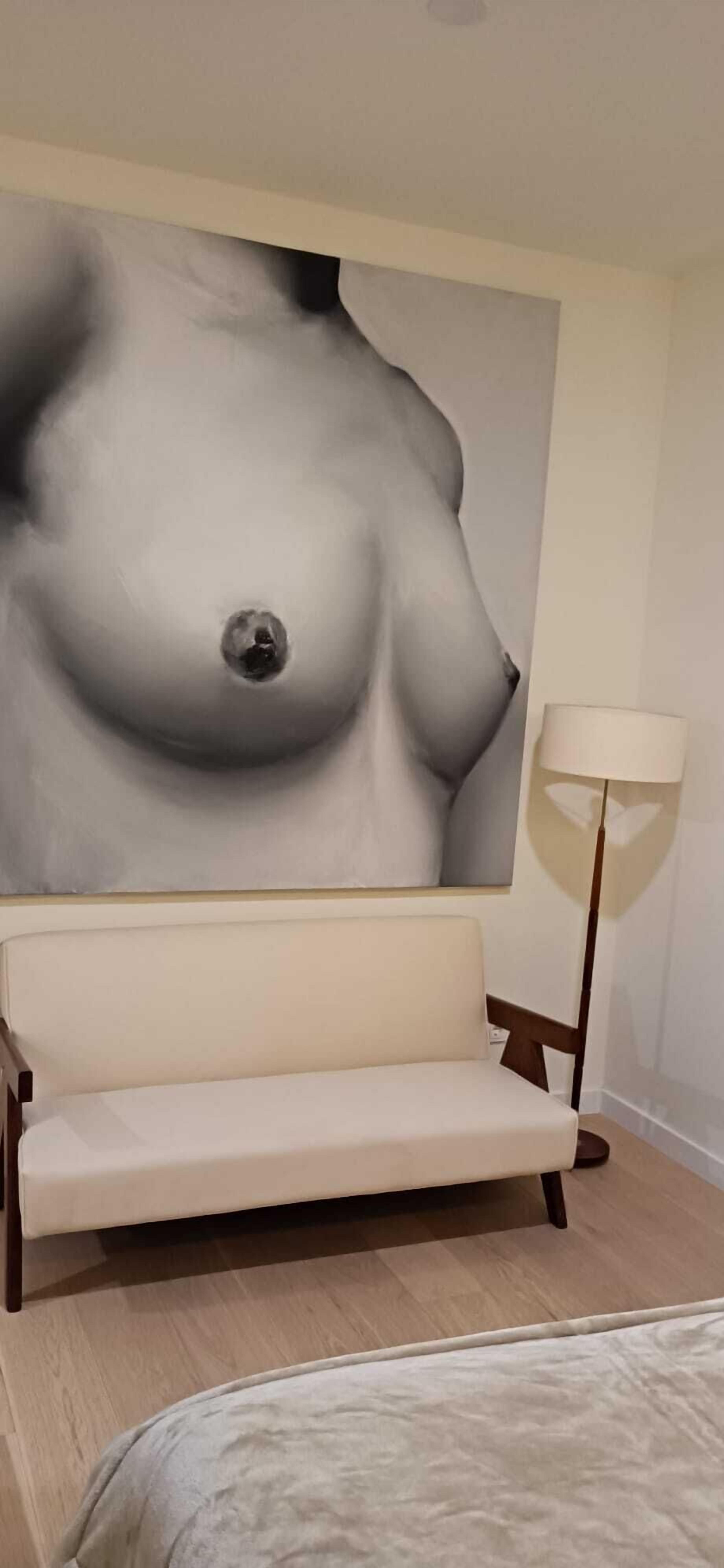 A room with a large abstract painting on the wall, a sofa, a lamp, and a bed.