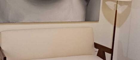 A room with a large abstract painting on the wall, a sofa, a lamp, and a bed.