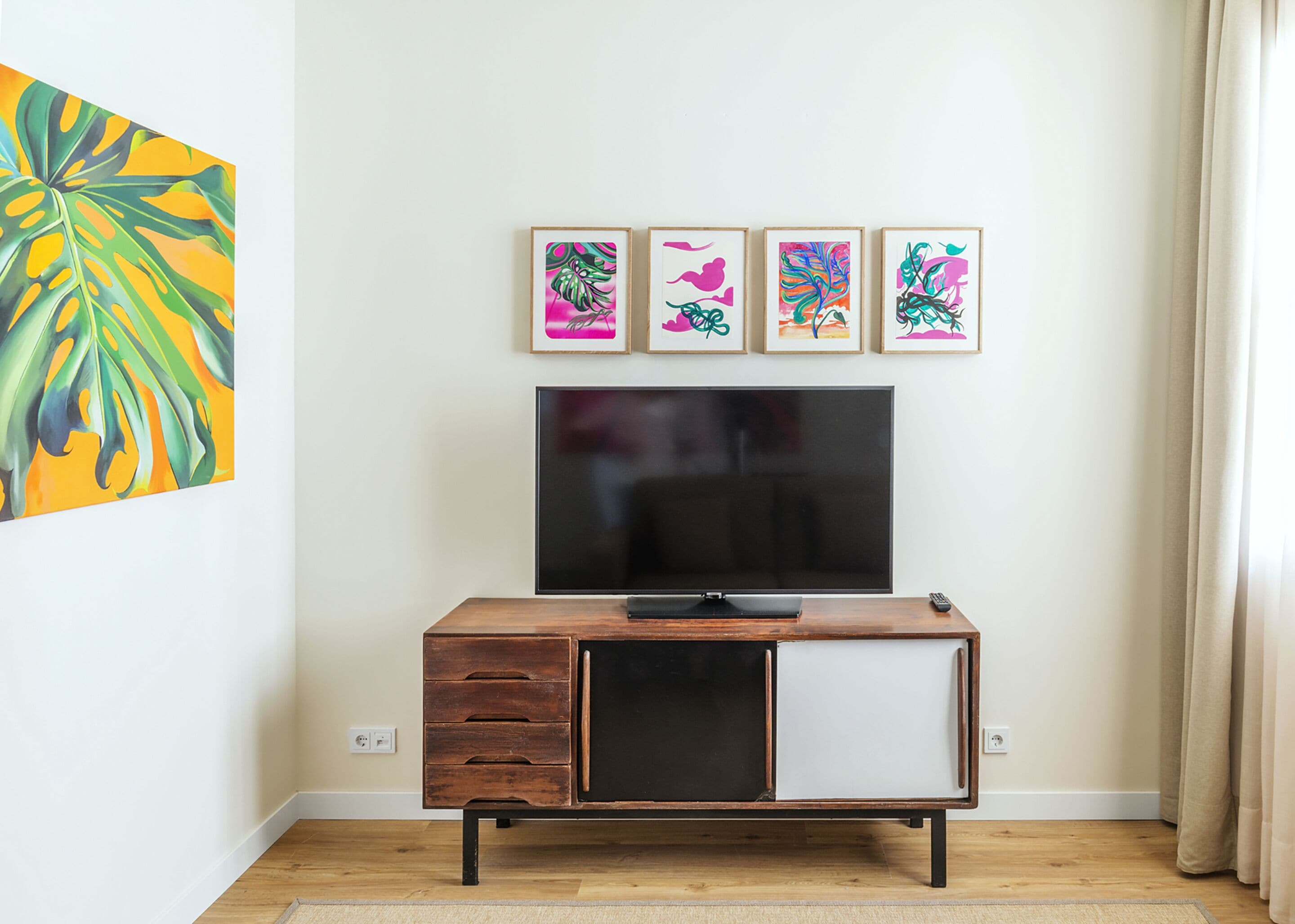 Une pièce comprenant un meuble en bois, un téléviseur à écran plat et quatre œuvres d’art encadrées accrochées au mur.